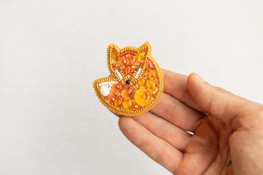 a hand is holding a beaded fox brooch