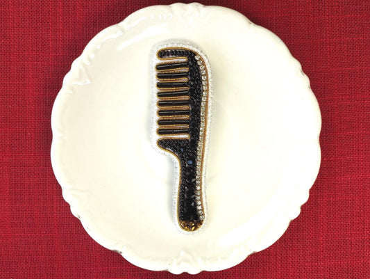 A white plate with a black and gold comb-like object placed on it, set against a red background.
