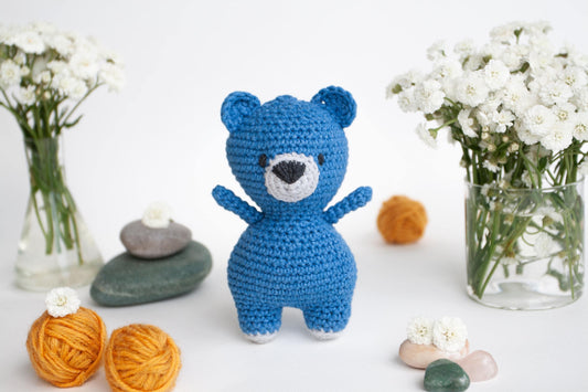 a crocheted teddy bear next to a vase of flowers