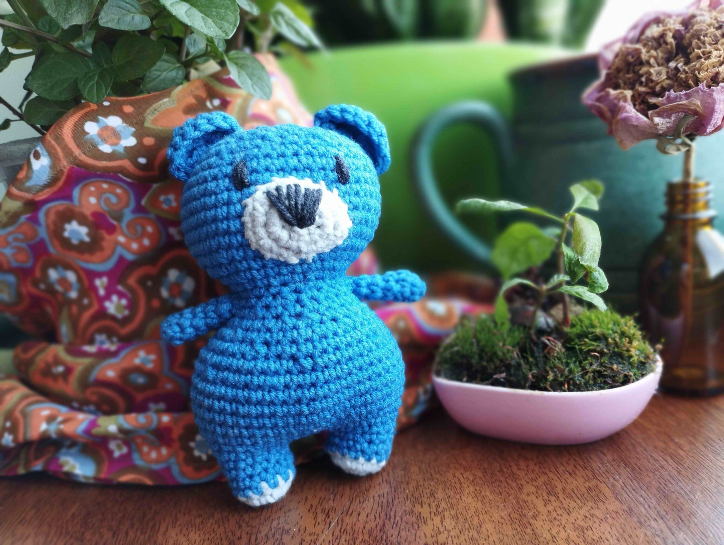 a crocheted blue teddy bear next to a potted plant