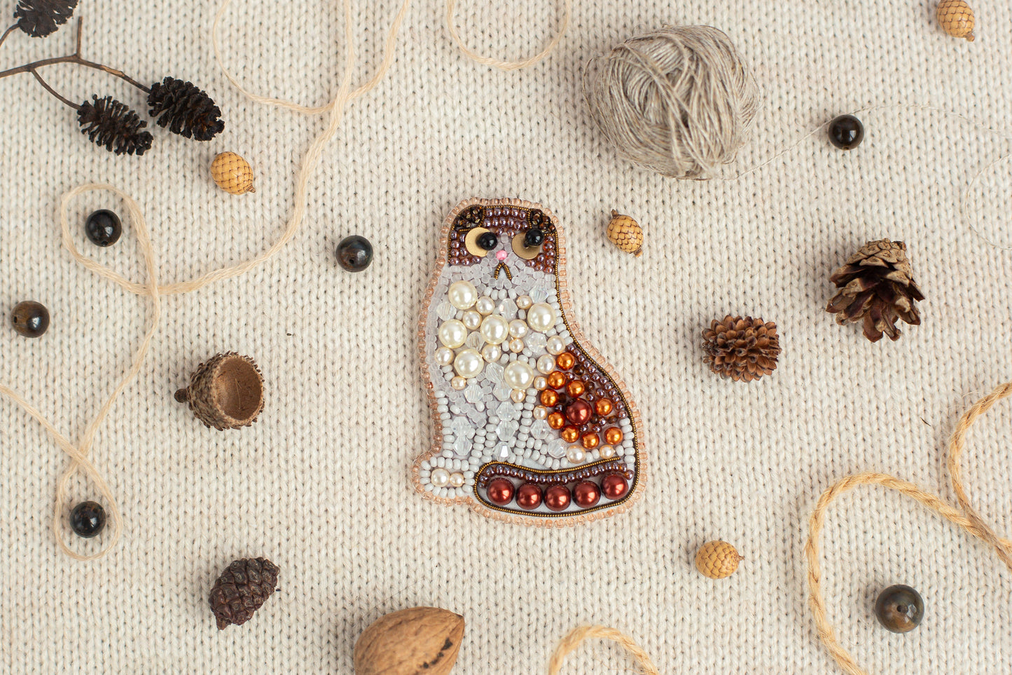 a mosaic of various objects, including a cat-shaped piece of art, pine cones, beads, and other natural elements, all arranged on a white background.
