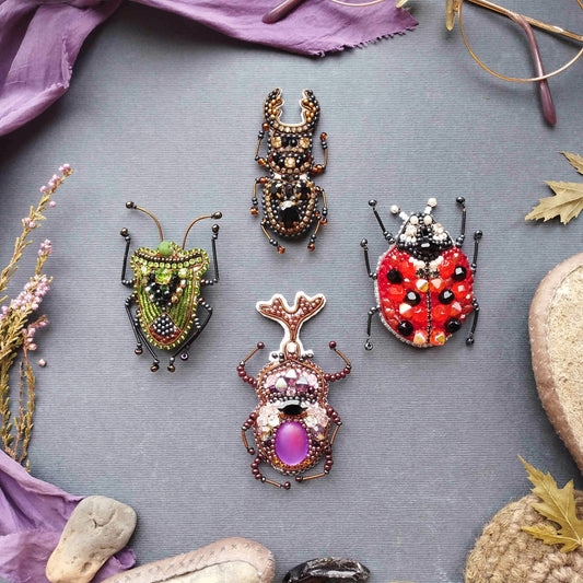 four intricately designed insect brooches, each with unique colors and patterns, arranged on a gray background.