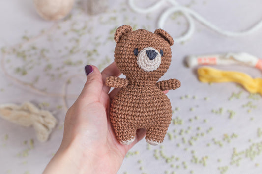 a hand holding a small crocheted teddy bear