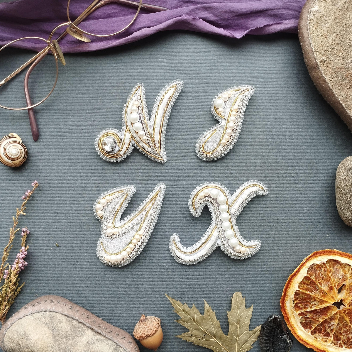 a collection of decorative objects arranged on a grey background, including a pair of glasses, a necklace, a leaf, a nut, a piece of fruit, and a stone.