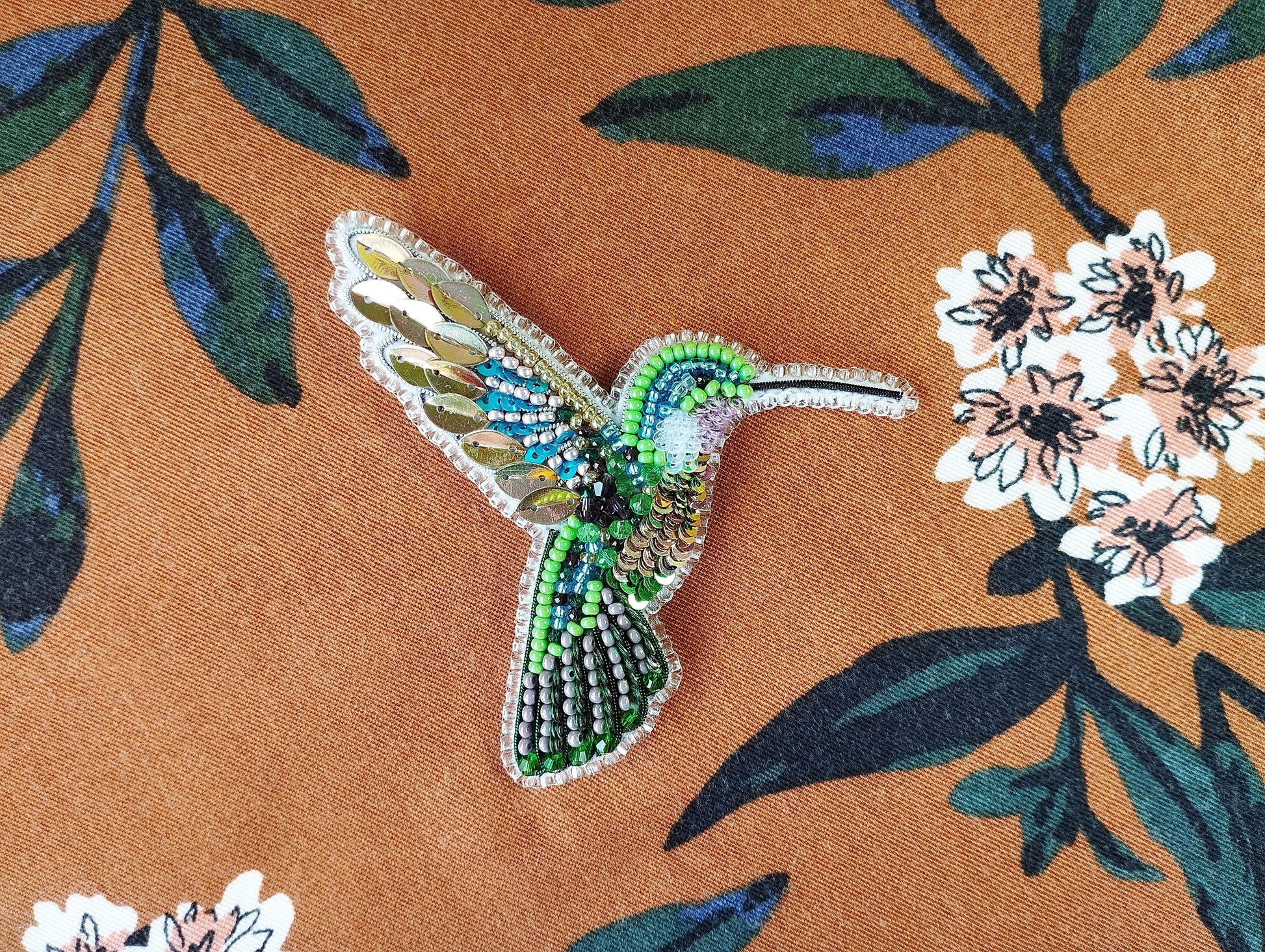 a beaded hummingbird sitting on a flowered fabric