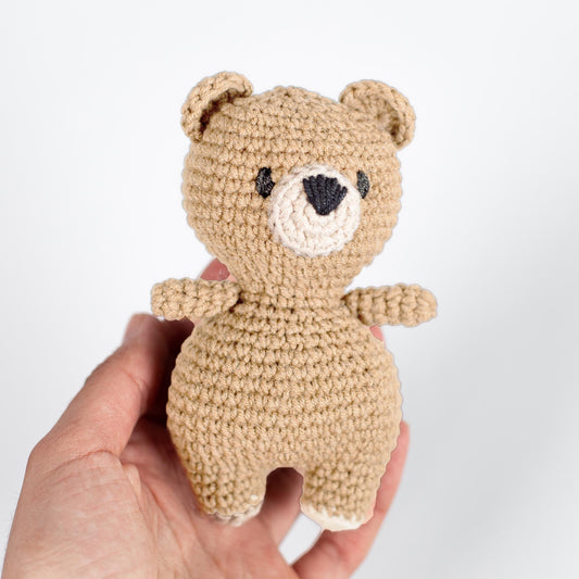 a hand holding a small crocheted teddy bear