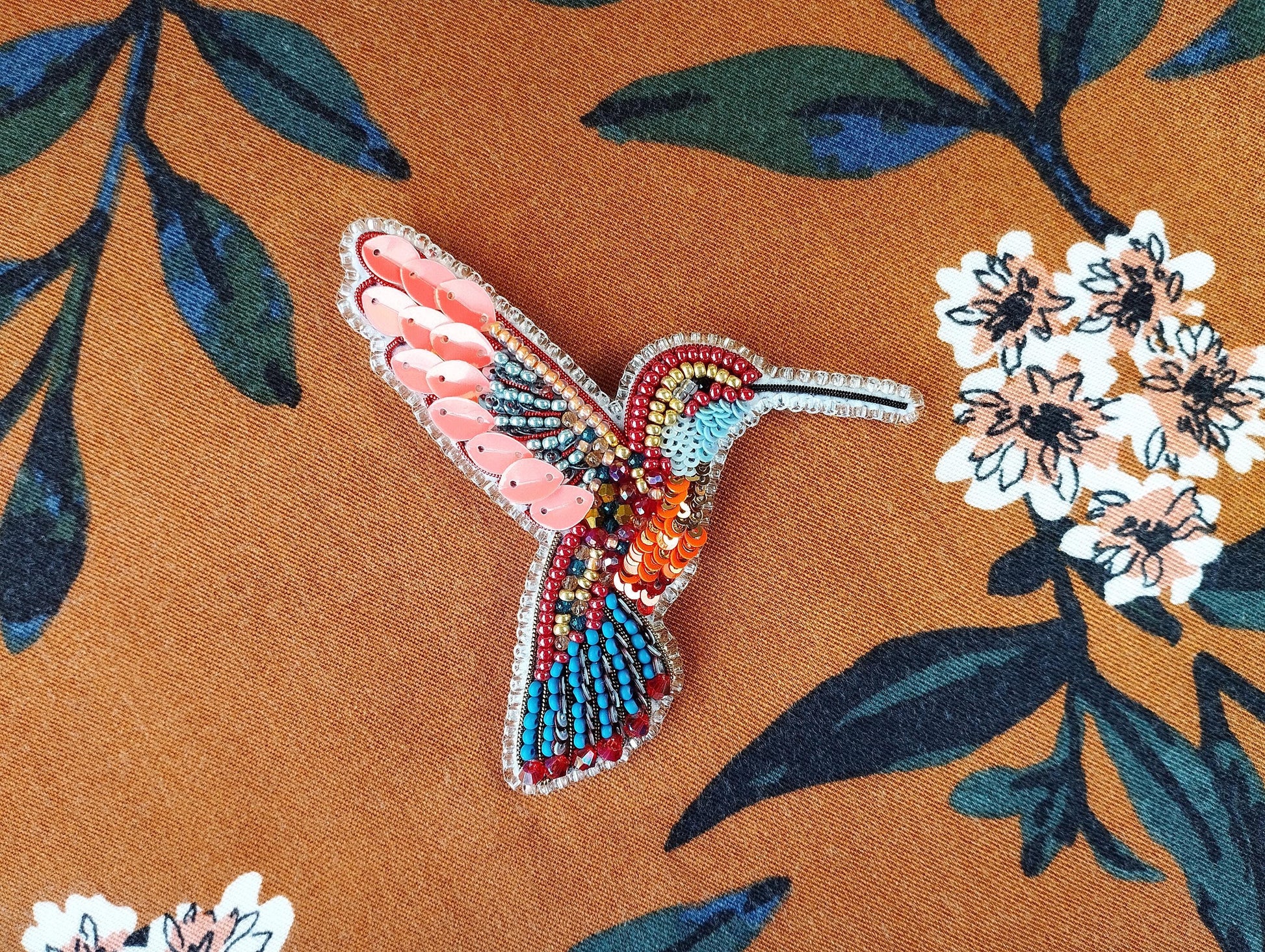 a colorful bird brooch sitting on top of a flowery fabric