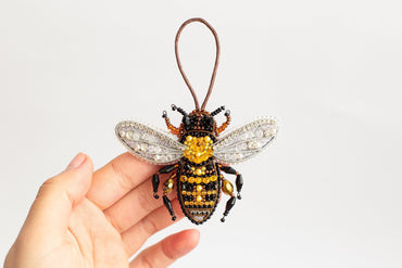 a hand holding a beaded bee ornament