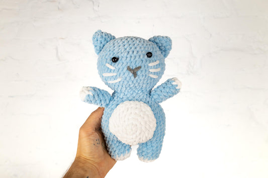 a hand holding a small blue crocheted cat