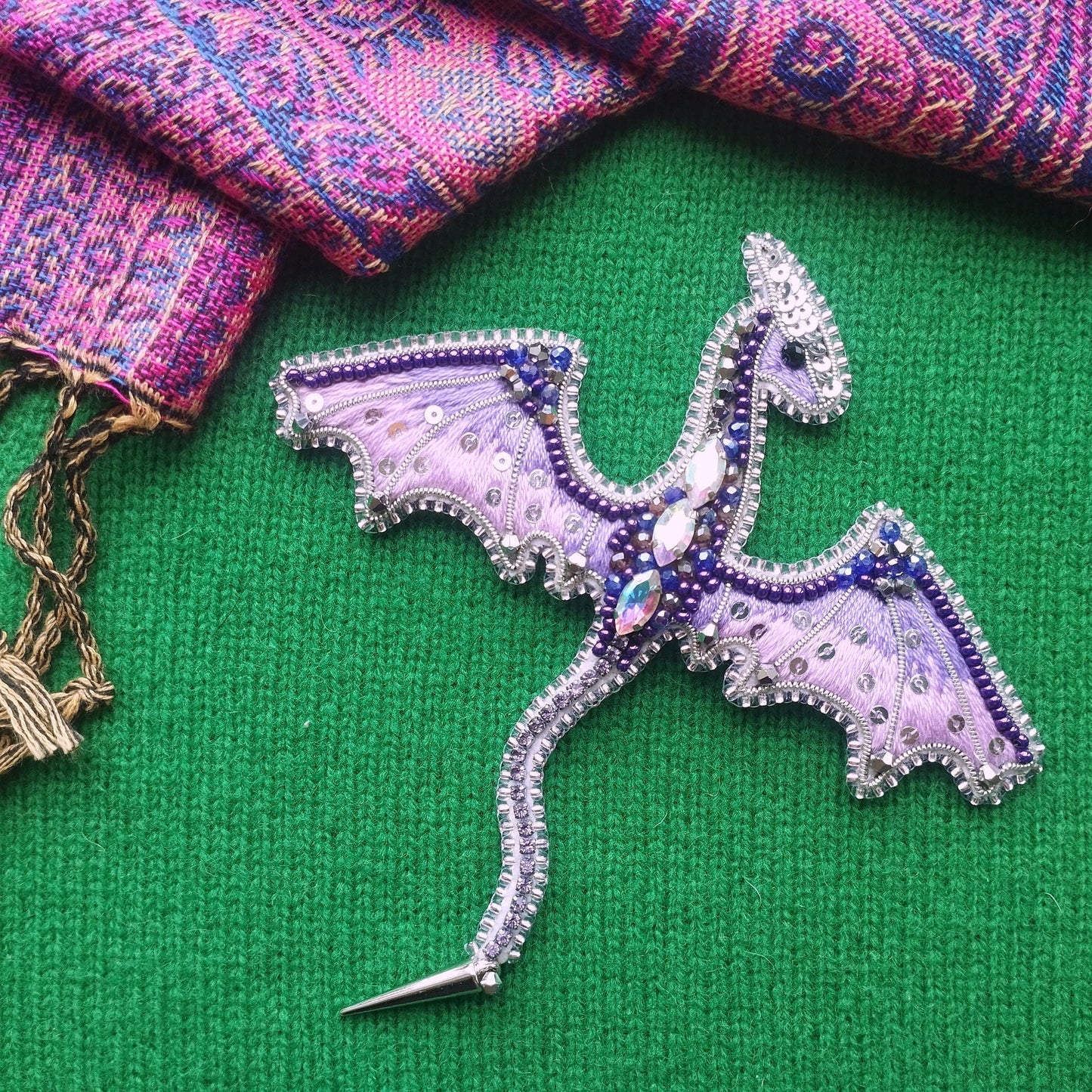 a decorative dragon pin with a green background and a pink and purple patterned fabric.