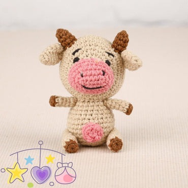 a small toy cow sitting next to a ball of yarn