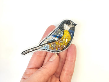 a hand holding a small bird brooch in it's left hand