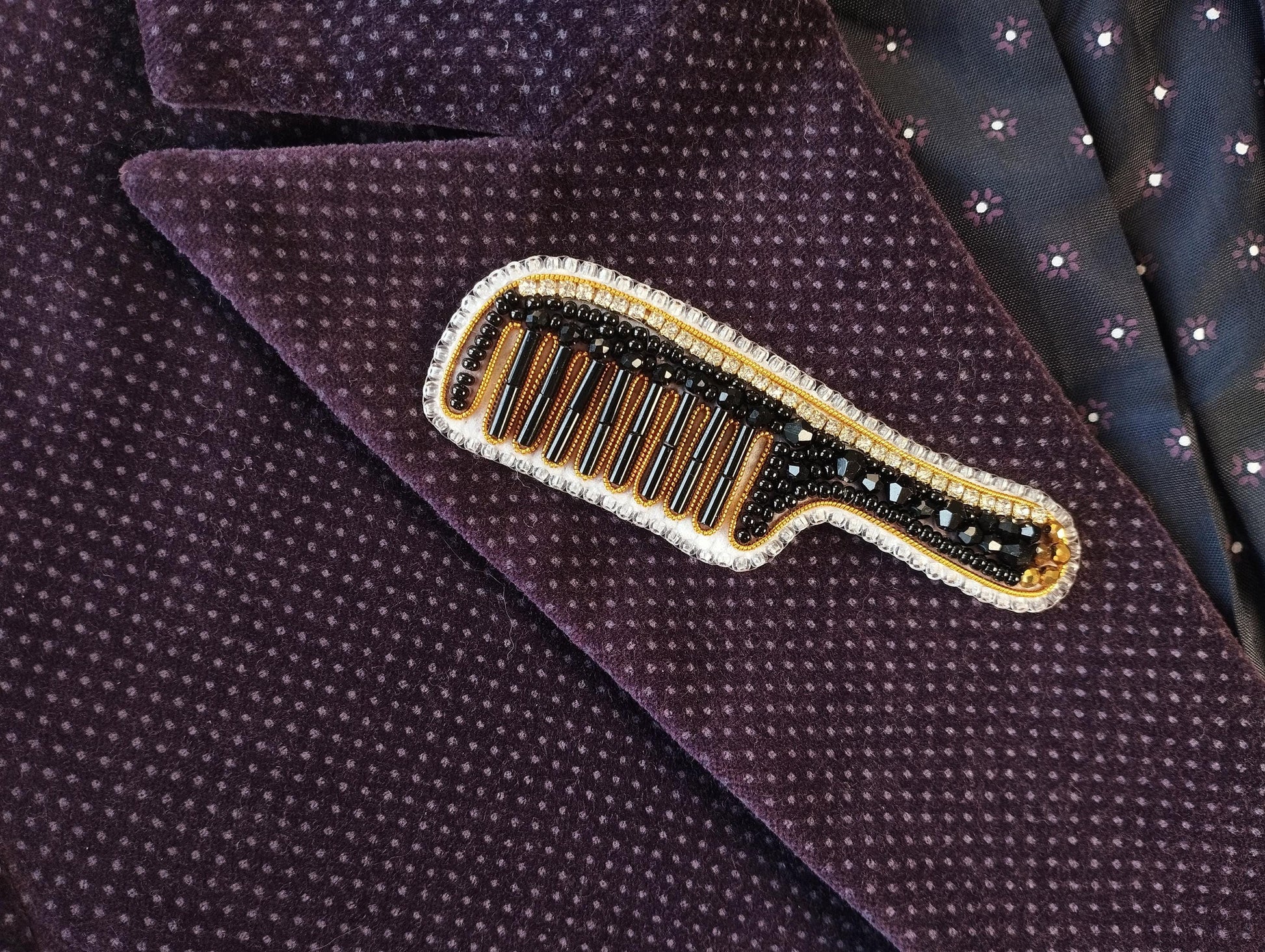 A close-up image of a purple fabric with a decorative comb pin featuring a gold and black design, placed on the fabric.