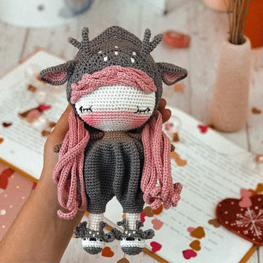 a crocheted cow with a pink scarf on it's head
