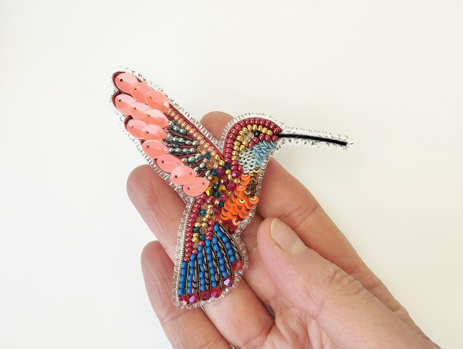 a hand holding a colorful beaded bird brooch