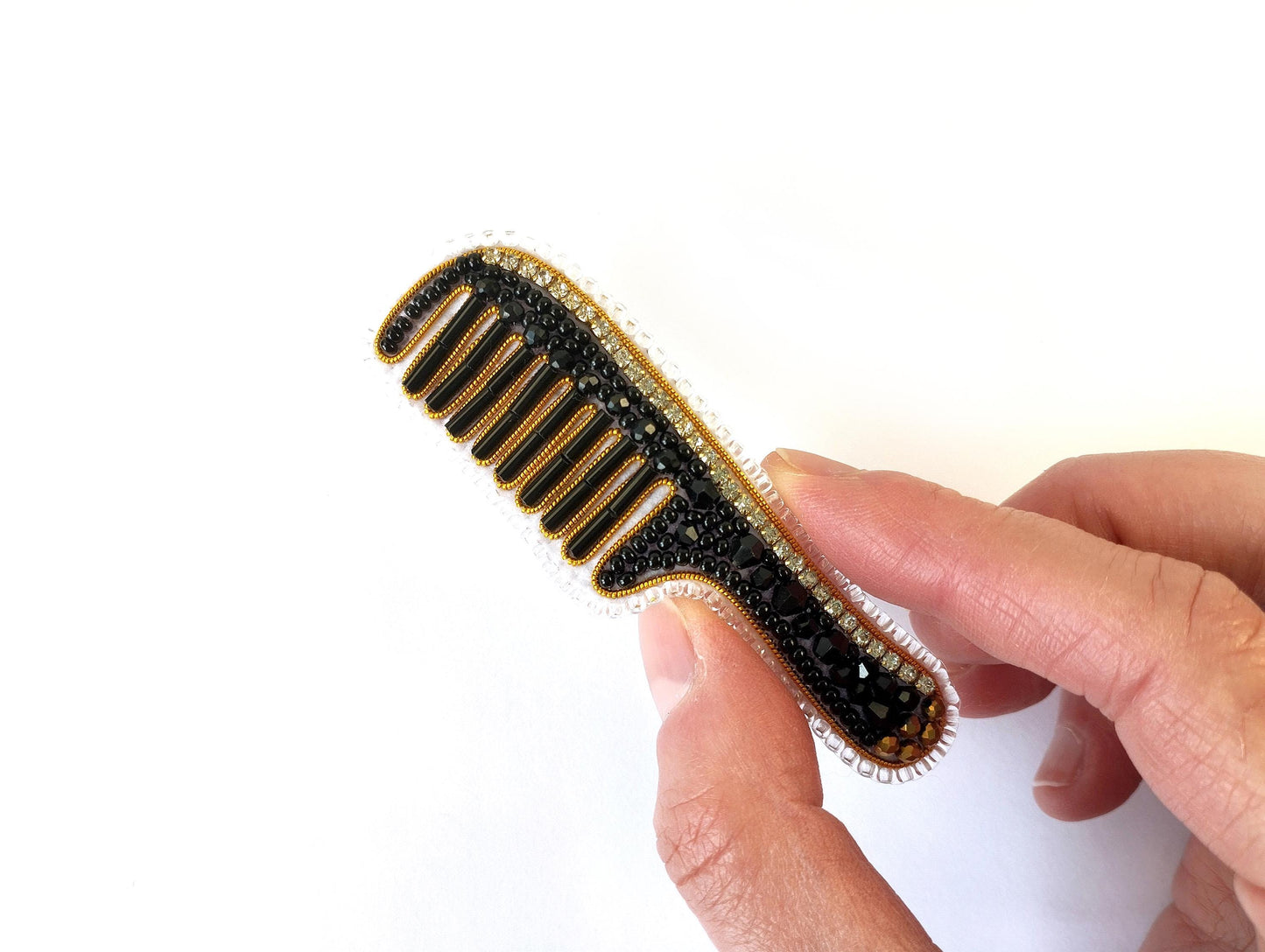 A hand holding a black and gold comb with rhinestones or crystals on it.