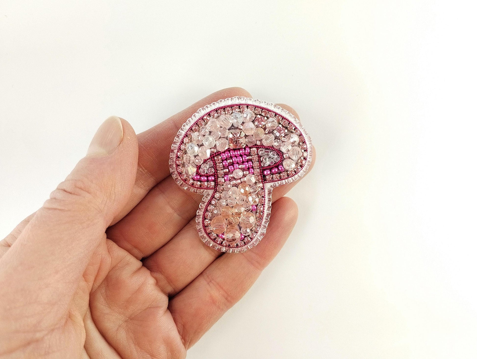 a hand holding a pink and white brooch