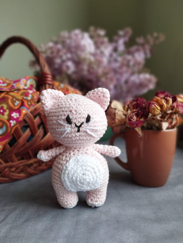 a crocheted cat sitting next to a basket of flowers