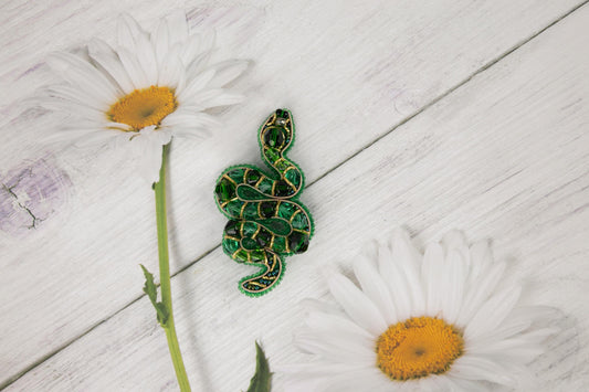 a green snake on a white wooden surface next to daisies