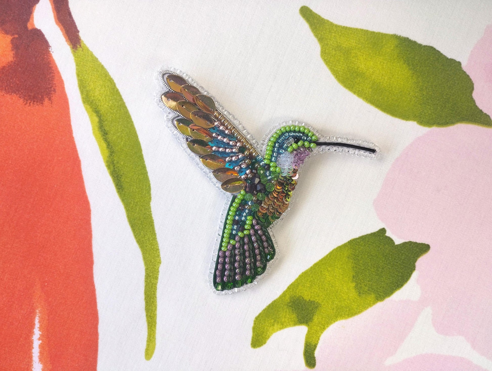 a beaded hummingbird brooch sits on a floral background