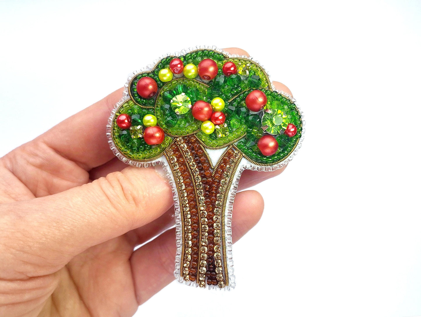 a hand holding a brooch with a tree on it