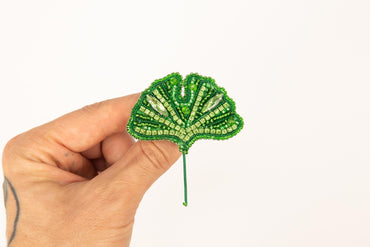 a hand holding a green beaded leaf