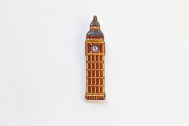 a brooch with a clock on it on a white surface