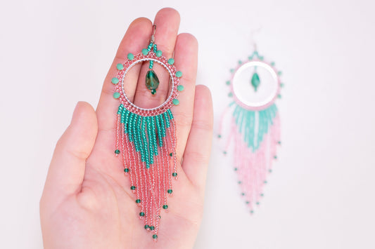 a pair of pink and green beaded earrings hanging from a tree branch