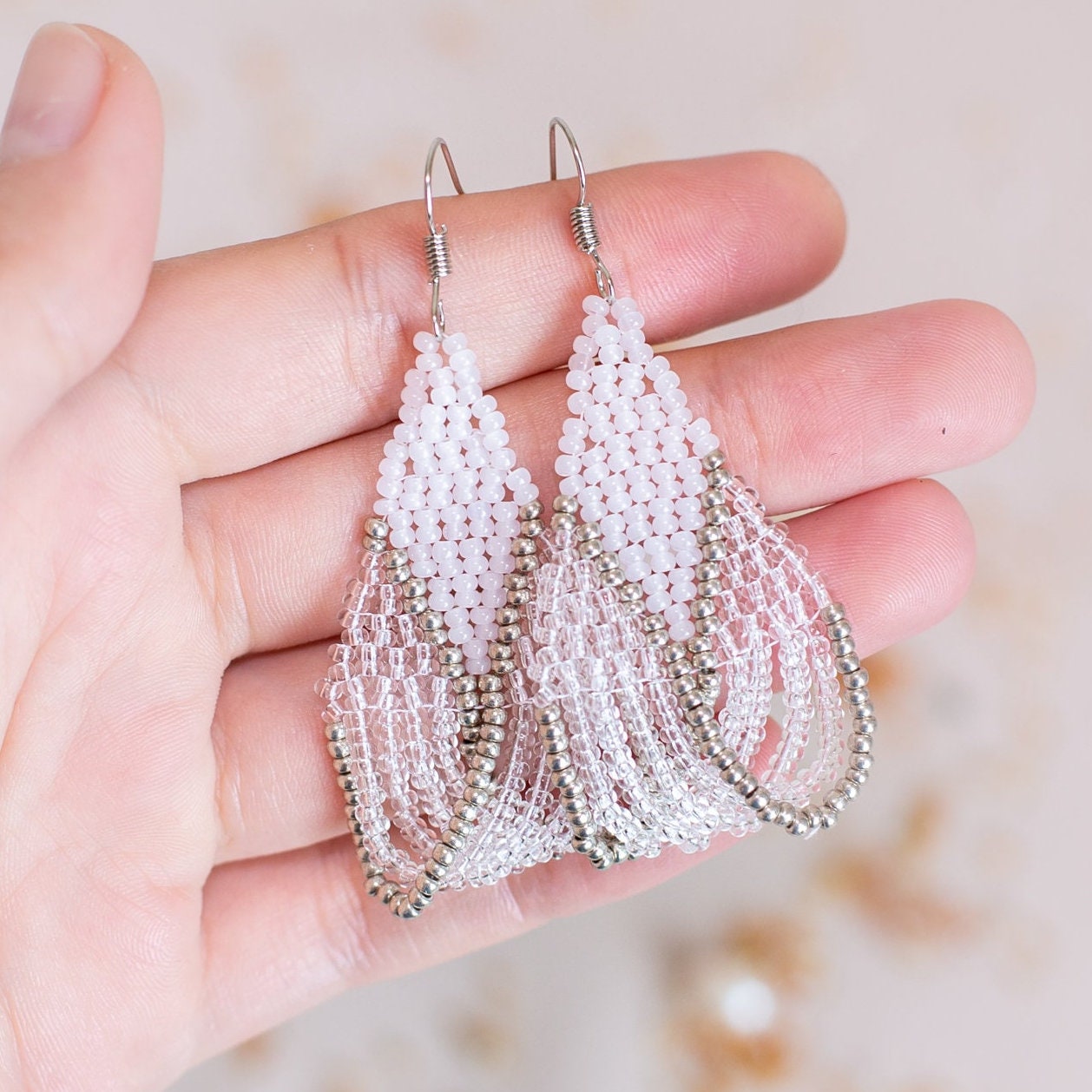 a pair of white beaded earrings on a pink background