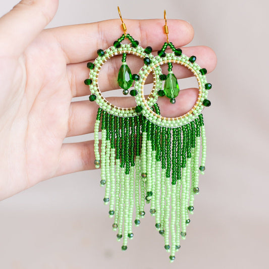 a pair of green beaded earrings hanging from a tree branch