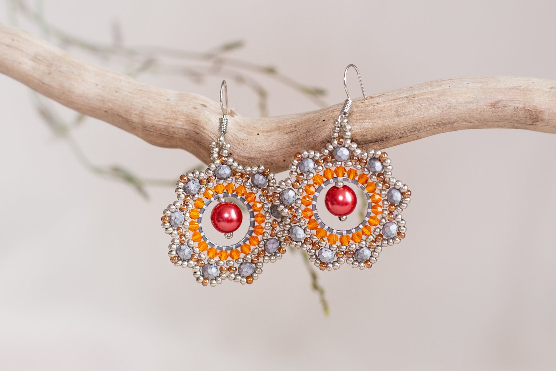 a pair of orange and silver earrings hanging from a branch