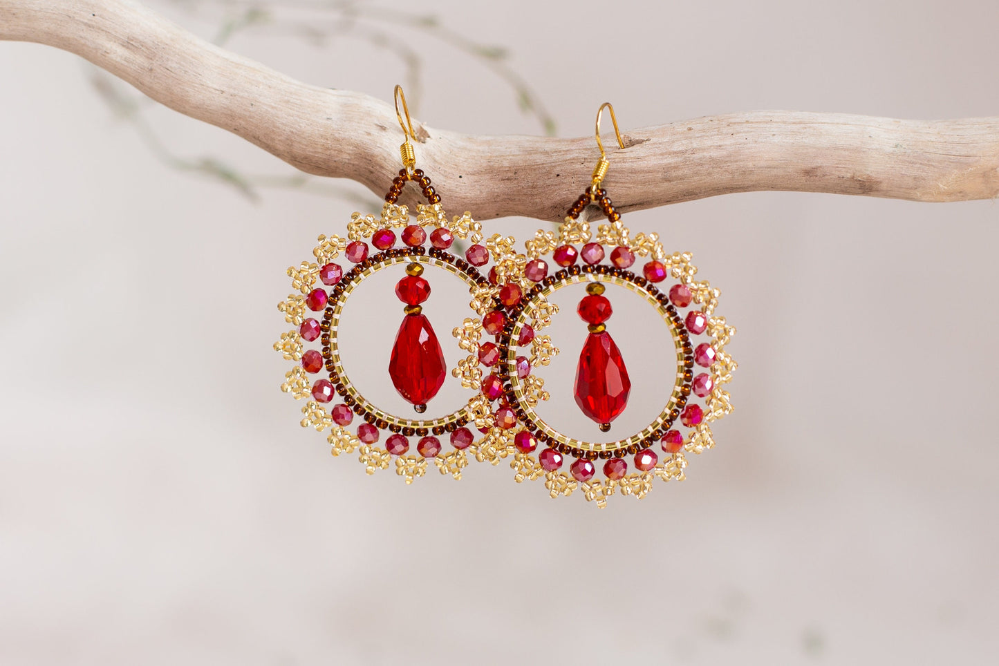 a pair of red and gold earrings hanging from a tree branch