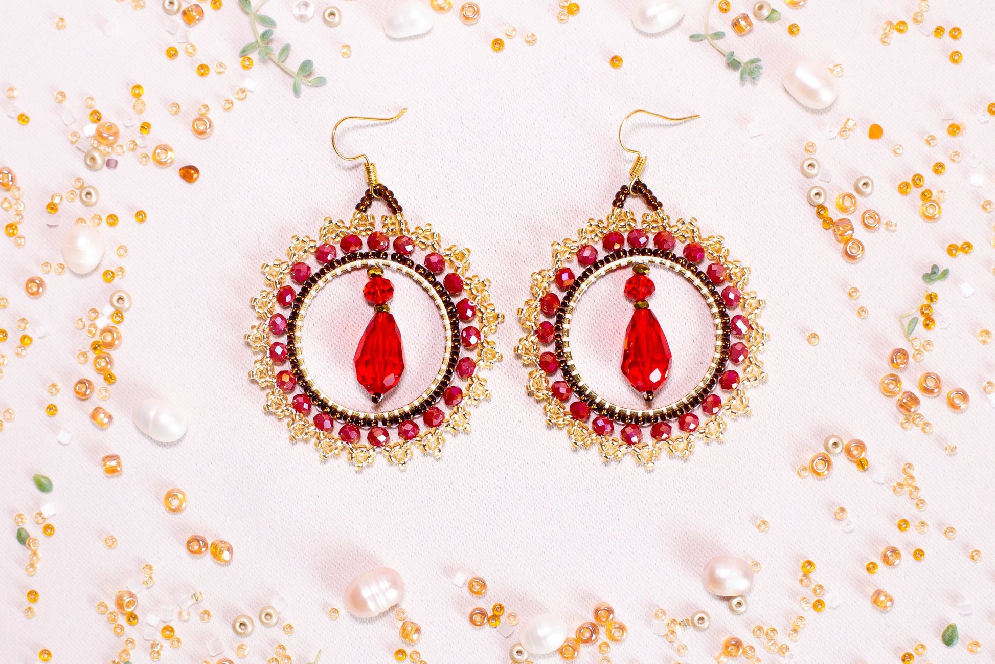 a pair of red and gold earrings on a white surface