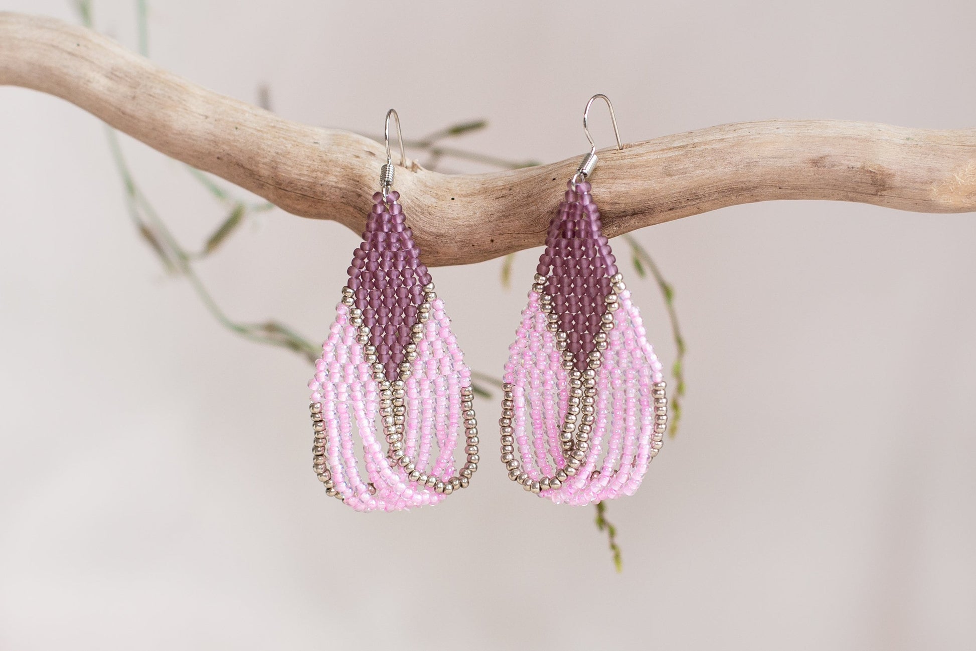 a pair of pink and purple beaded earrings hanging from a branch