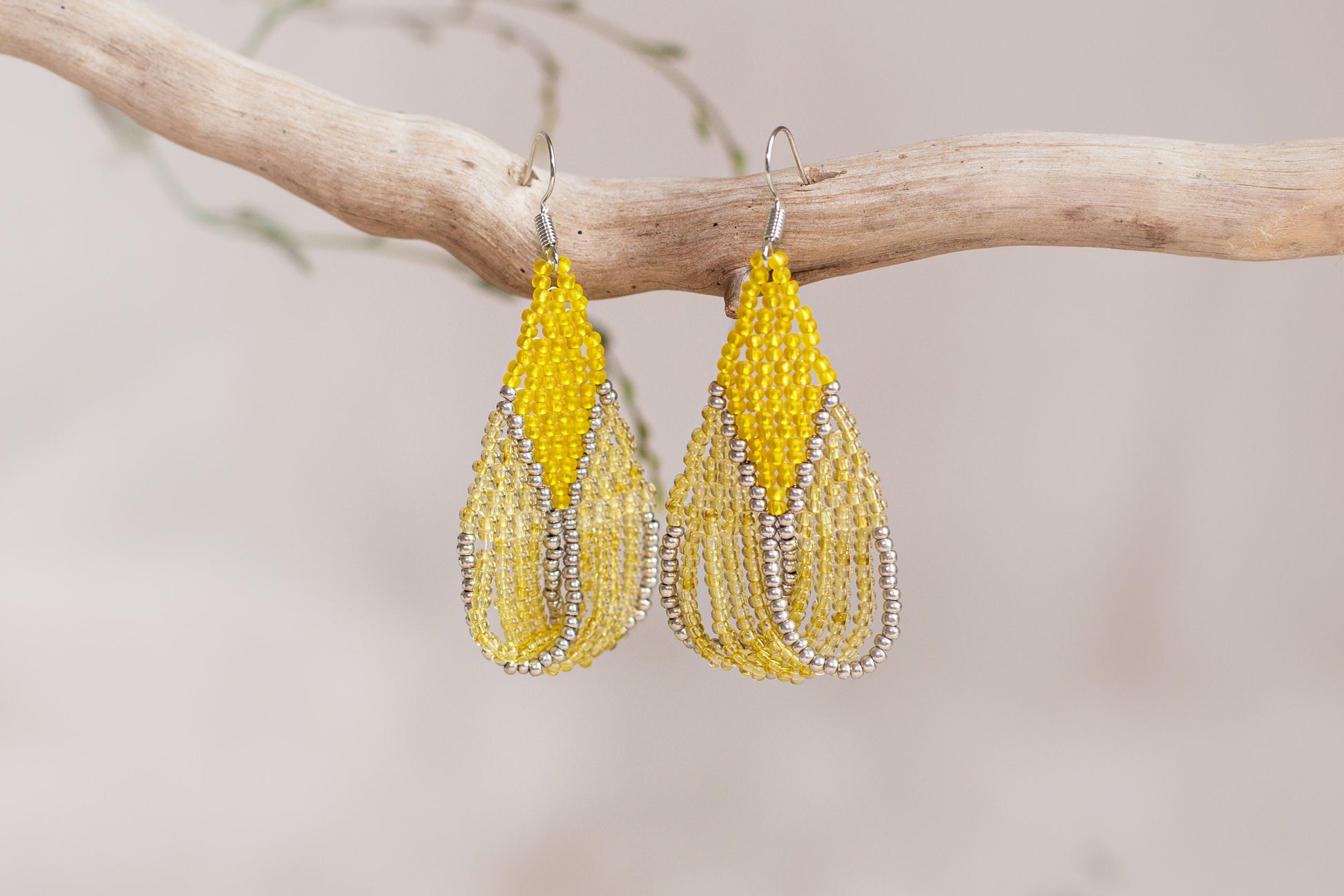a pair of yellow beaded earrings hanging from a tree branch