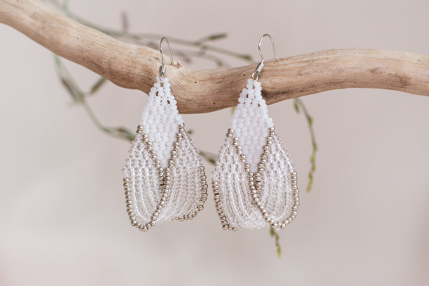 a pair of white beaded earrings hanging from a branch