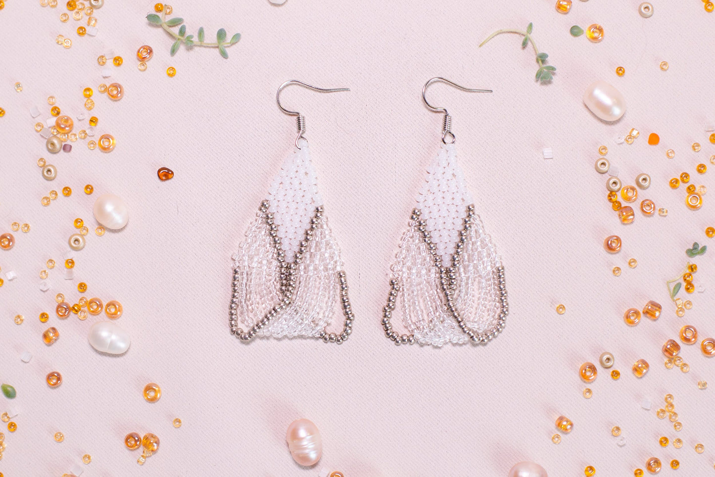 a pair of white beaded earrings on a pink background