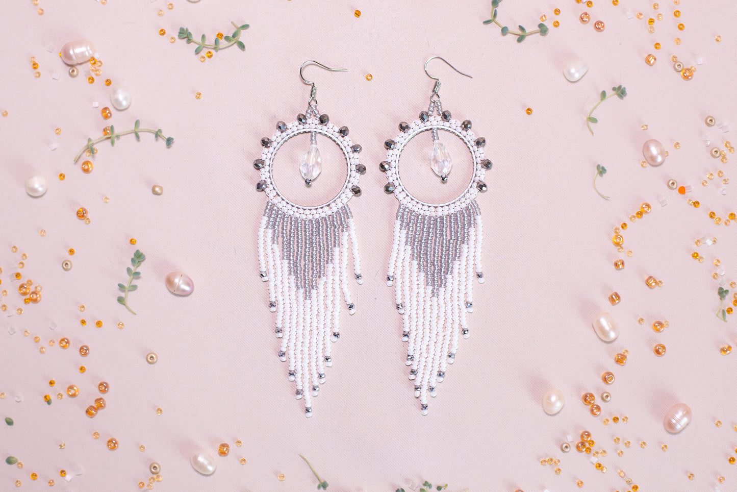 a pair of white beaded earrings on a pink background
