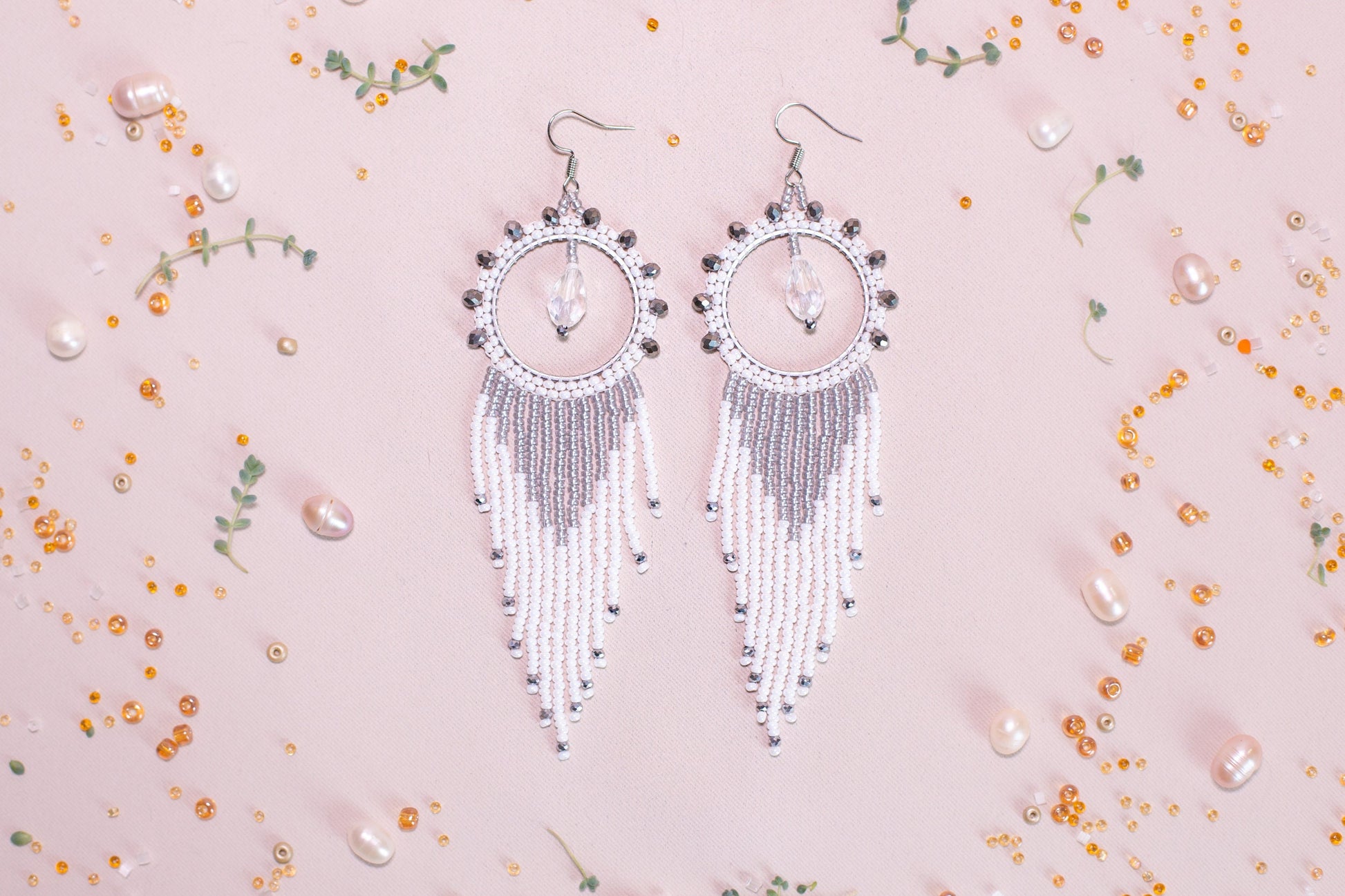 a pair of white beaded earrings on a pink background