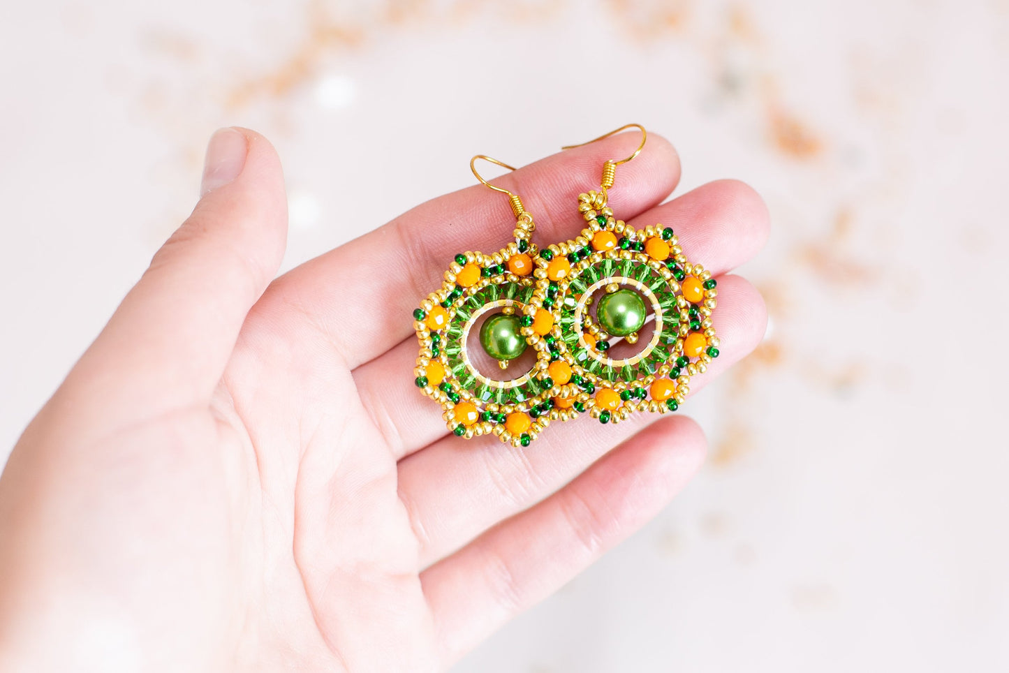a hand holding a green and yellow beaded earrings
