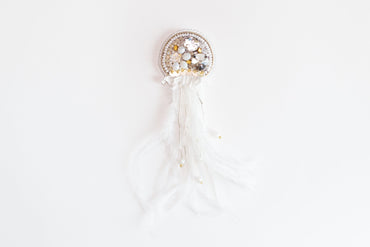 a white brooch with a white feather and beads
