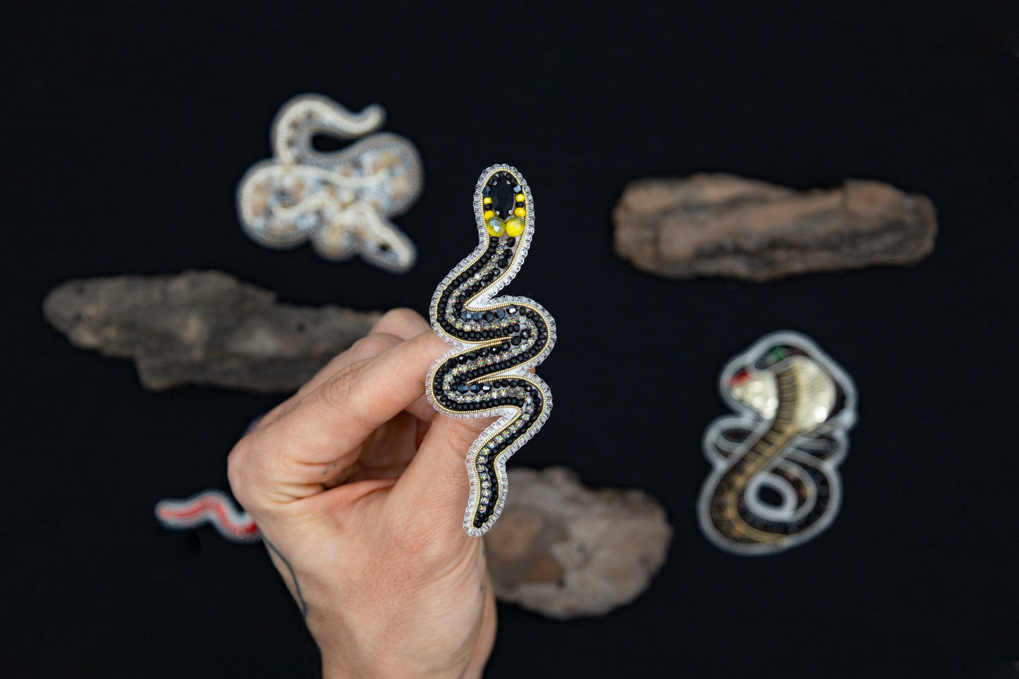 a hand is holding a beaded snake on a black surface