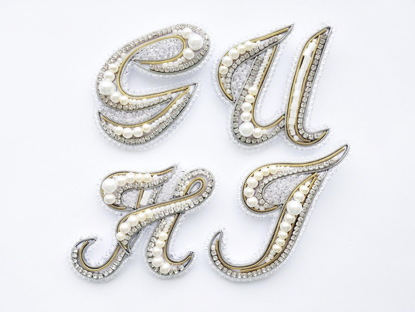 four decorative pieces made of gold, silver, and pearl materials, arranged in a square formation against a white background.