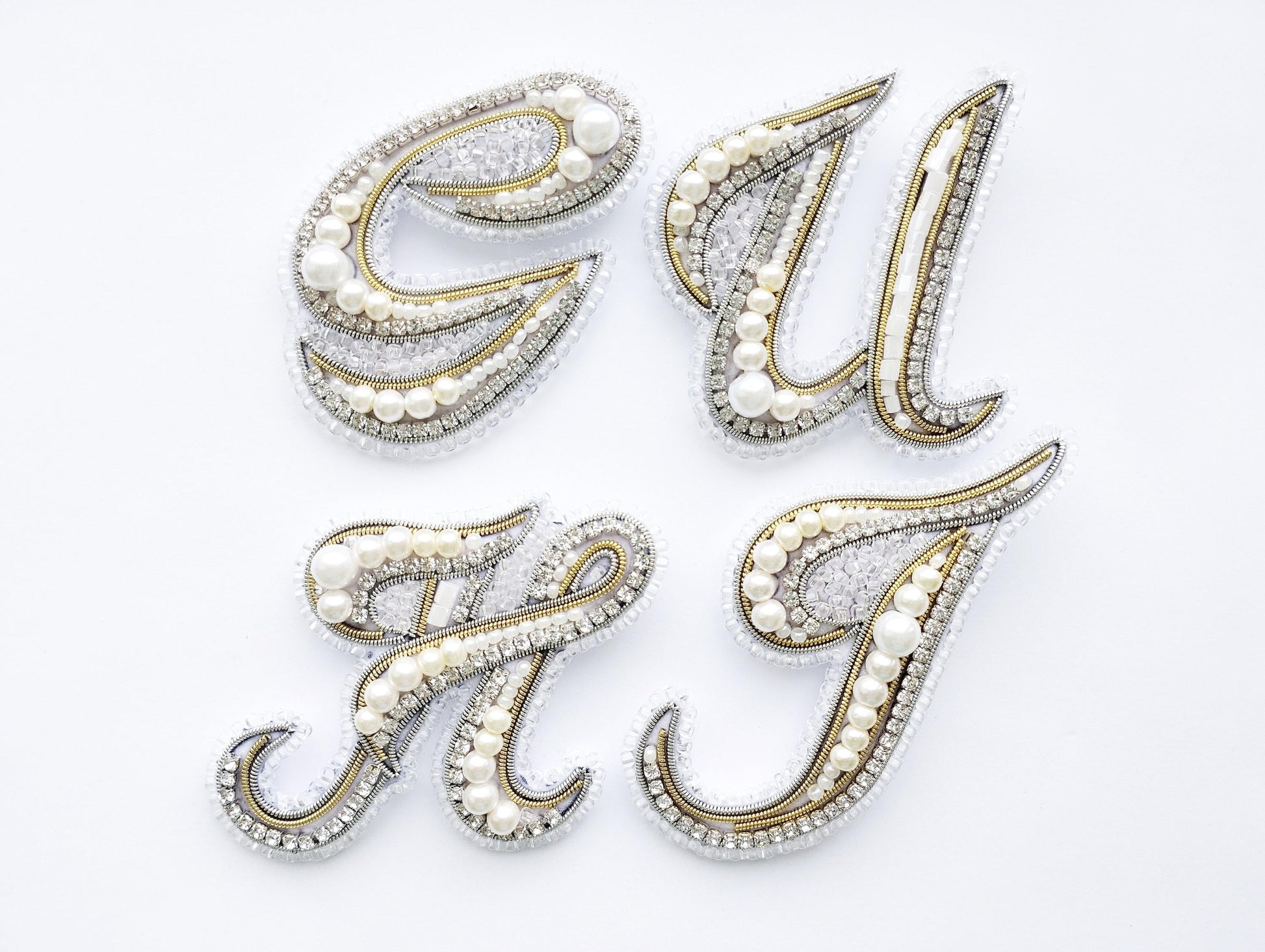 four decorative pieces made of gold, silver, and pearl materials, arranged in a square formation against a white background.