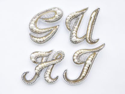 four decorative pieces made of gold, silver, and pearl materials, arranged in a square formation against a white background.