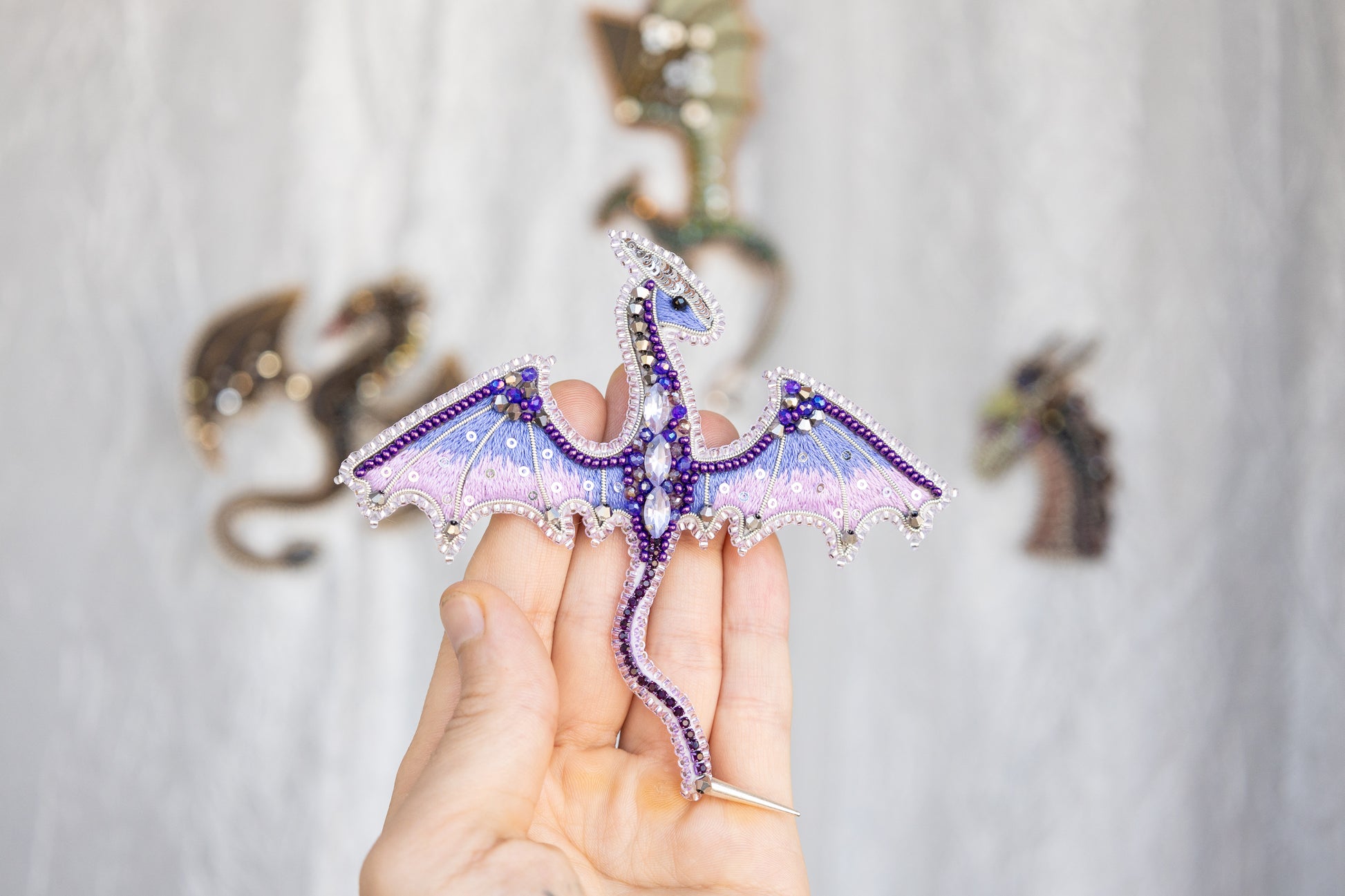 A hand holding a decorative dragon pin with intricate beading and gemstone details.