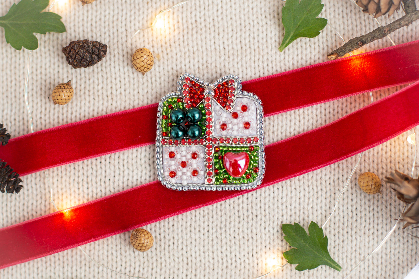 a red ribbon with a decorative piece on it, surrounded by Christmas-themed items such as pine cones, leaves, and lights.