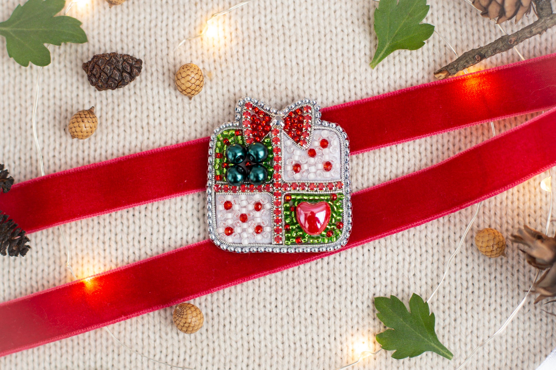 a red ribbon with a decorative piece on it, surrounded by Christmas-themed items such as pine cones, leaves, and lights.