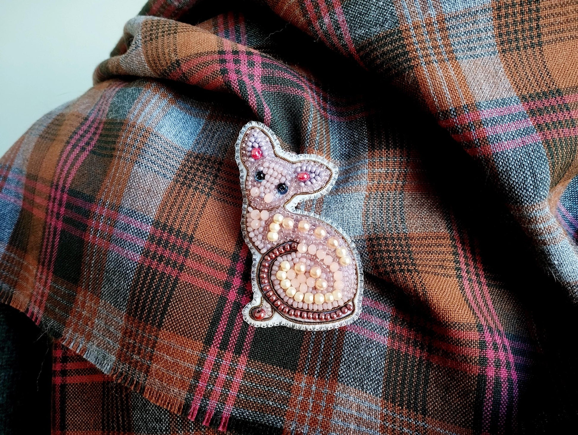 A close-up image of a decorative cat brooch or pin placed on a plaid fabric.