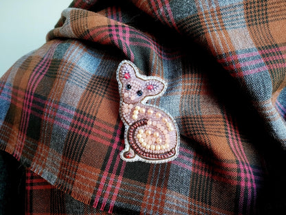 A close-up image of a decorative cat brooch or pin placed on a plaid fabric.